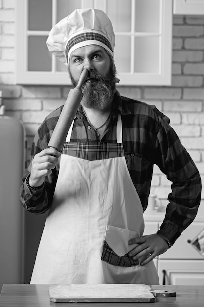 Chef barbudo enfia um rolo no nariz Chef louco em uma cozinha branca Foto muito engraçada