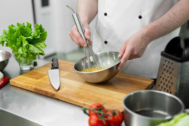 El chef bate los huevos con las manos en un bol para hacer una tortilla con verduras