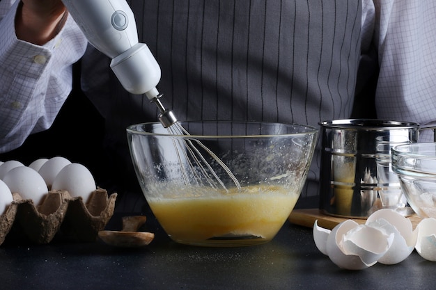 Chef con batidora en manos cocinando pastel con ingredientes en la mesa