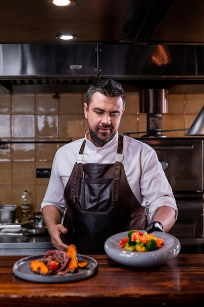 Chef bonito com avental de couro em pé no balcão servindo pratos em restaurante