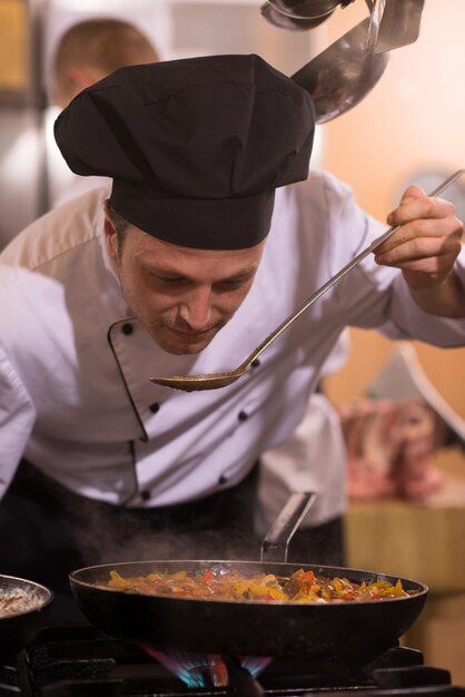 Chef bonito degustando comida com colher na cozinha do restaurante