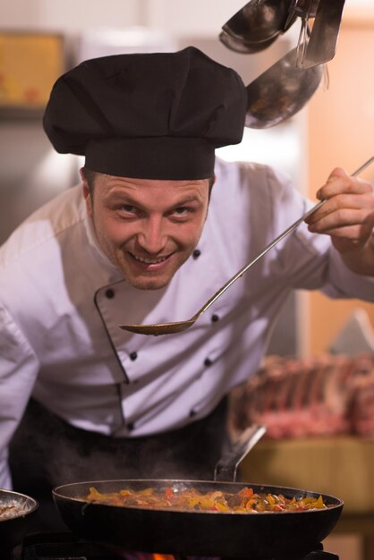 Chef bonito degustando comida com colher na cozinha do restaurante