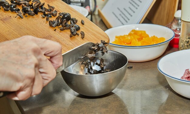 El chef cambia las aceitunas a la ensalada con naranjas de calabacín y salami Cocina gourmet francesa sobre fondo de madera