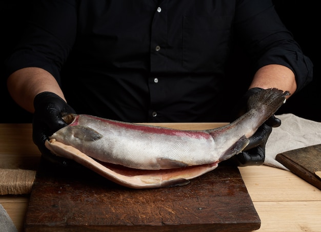 Chef con una camisa negra y guantes de látex negro sostiene una carcasa cruda de salmón sin cabeza