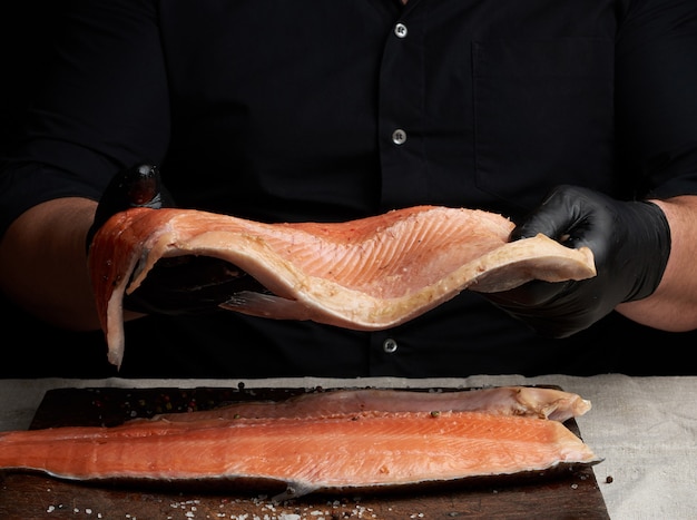 Chef con una camisa negra y guantes de látex negro sostiene un gran trozo de filete de salmón