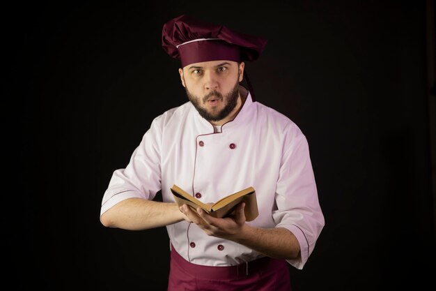 Chef chocado homem de uniforme mantém livro de receitas