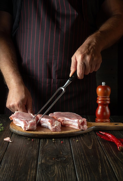 El chef cocina el almuerzo con bistecs de carne cruda en rodajas en la tabla de cortar de la cocina del restaurante