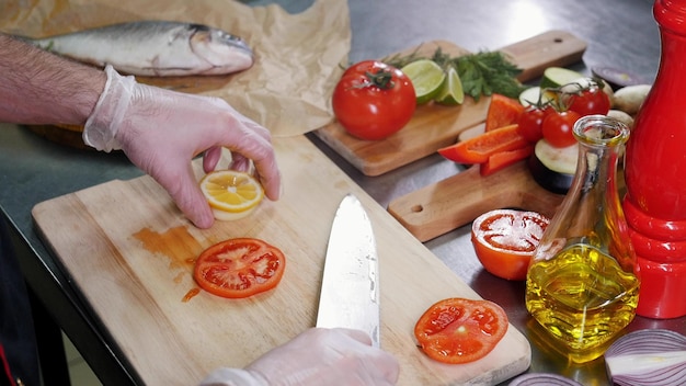 Un chef en la cocina cortando tomate y limón.