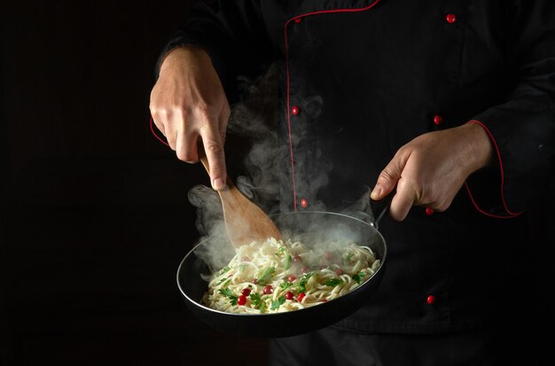 El chef cocina espaguetis en una sartén caliente Espacio para publicidad en un fondo negro Cocina nacional italiana