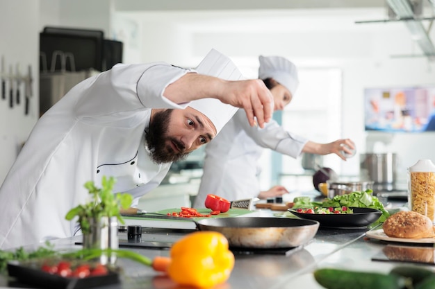 El chef de cocina gourmet adorna el plato de la cena con pimiento rojo mientras cocina para el servicio de cena en el restaurante. Experto en gastronomía preparando platos con verduras frescas y orgánicas en la cocina