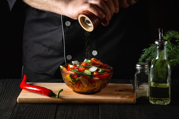 Chef en la cocina de un restaurante agrega pimientos a una ensalada de verduras frescas