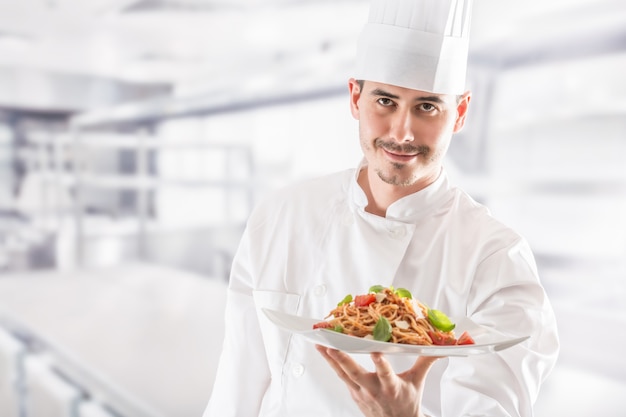 Chef en la cocina del restaurante con plato de comida italiana espaguetis a la boloñesa.