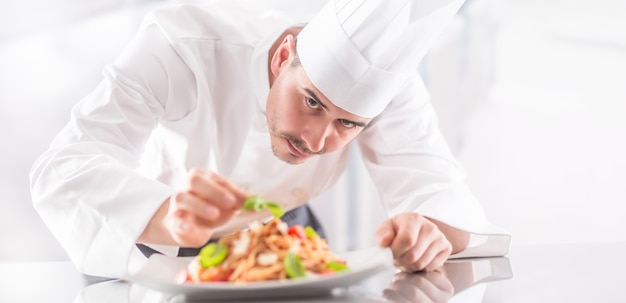 El chef en la cocina del restaurante prepara y decora la comida con las manos. Cocine preparando espaguetis a la boloñesa.