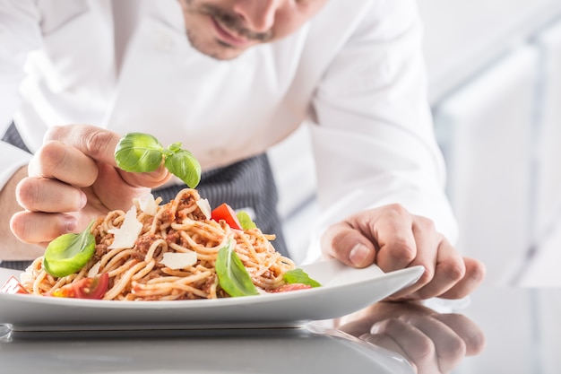 El chef en la cocina del restaurante prepara y decora la comida con las manos. Cocine preparando espaguetis a la boloñesa.