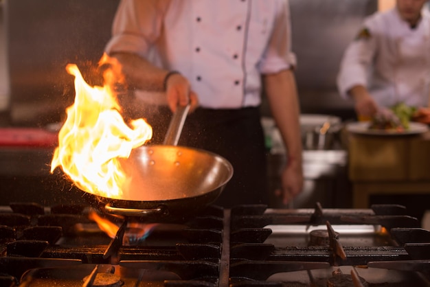 Chef cocinando y flambeando la comida en la cocina del restaurante