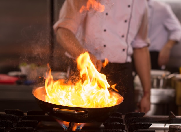 Chef cocinando y flambeando la comida en la cocina del restaurante