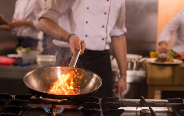 Chef cocinando y flambeando la comida en la cocina del restaurante