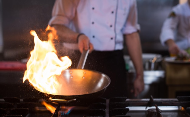 Chef cocinando y haciendo flambeado en la comida en la cocina del restaurante