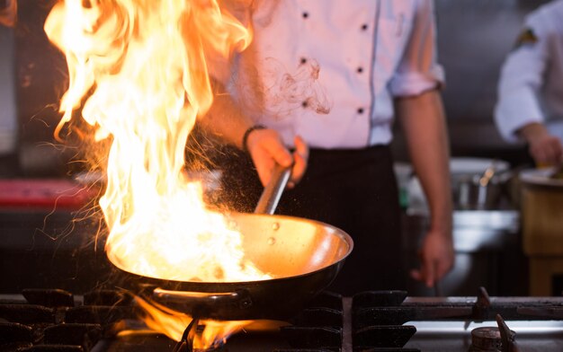 Chef cocinando y haciendo flambeado en la comida en la cocina del restaurante