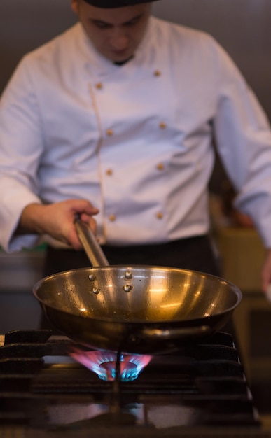 Chef cocinando y haciendo flambeado en la comida en la cocina del restaurante