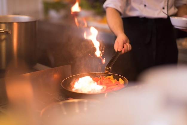 Chef cocinando y haciendo flambeado en la comida en la cocina del restaurante