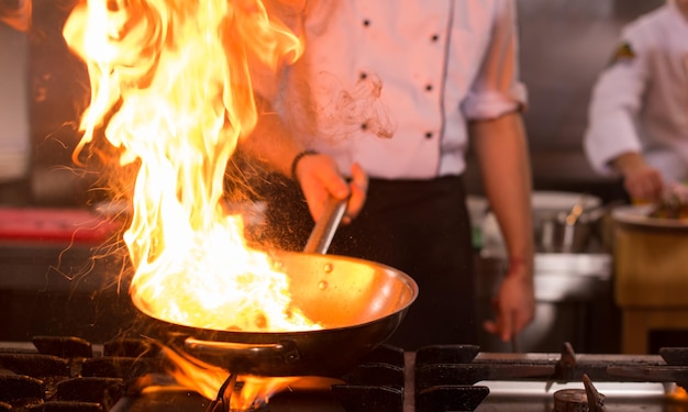 Chef cocinando y haciendo flambeado en la comida en la cocina del restaurante