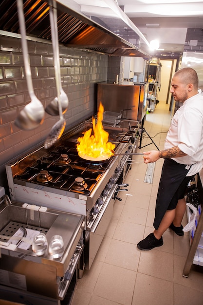 Foto chef cocinando con llama en una sartén sobre una estufa de cocina. en restaurante de cocina