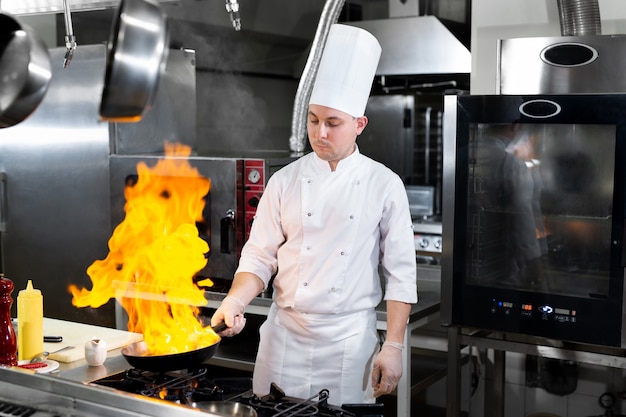 Chef cocinando con llama en una sartén sobre una estufa de cocina