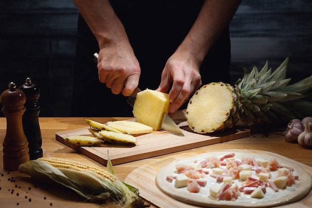 Chef cocinando pizza hawaiana, cortando piña fresca