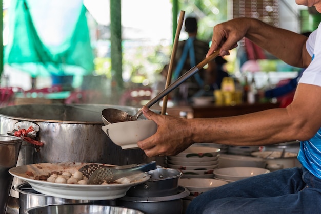 Foto chef cocinando una sopa de fideos en el mercado de comida de la calle