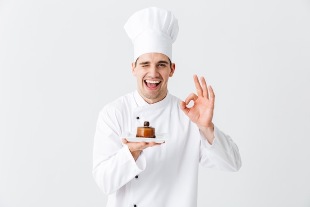 Chef cocinero hombre alegre vistiendo uniforme mostrando pasteles en un plato aislado sobre la pared blanca