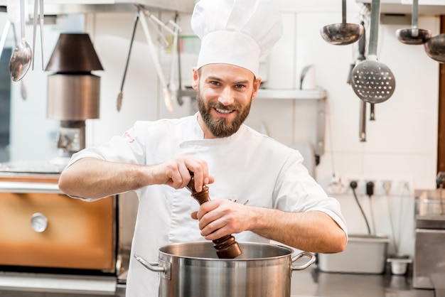 Chef cocinero en sopa de pimienta uniforme en la olla grande en la cocina del restaurante