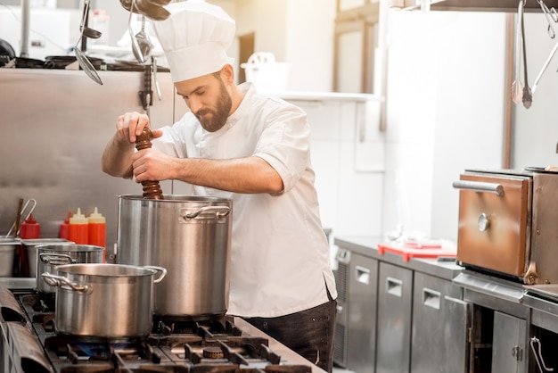 Chef cocinero en sopa de pimienta uniforme en la olla grande en la cocina del restaurante