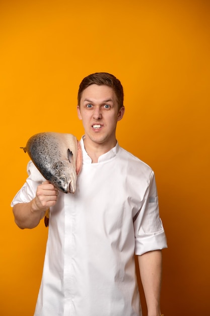 Chef cocinero sosteniendo un gran pez salmón atlántico en su hombro aislado sobre fondo amarillo