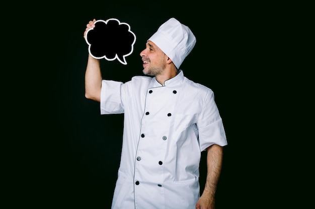 Chef cocinero vistiendo chaqueta y sombrero de cocina, sosteniendo una pizarra con discurso de burbuja cómica, sobre fondo negro