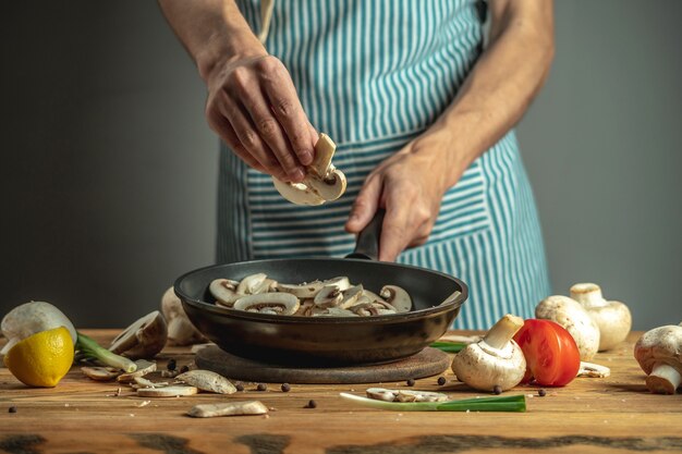 Chef coloque cogumelos frescos fatiados em uma frigideira. conceito do processo de cozimento de alimentos.