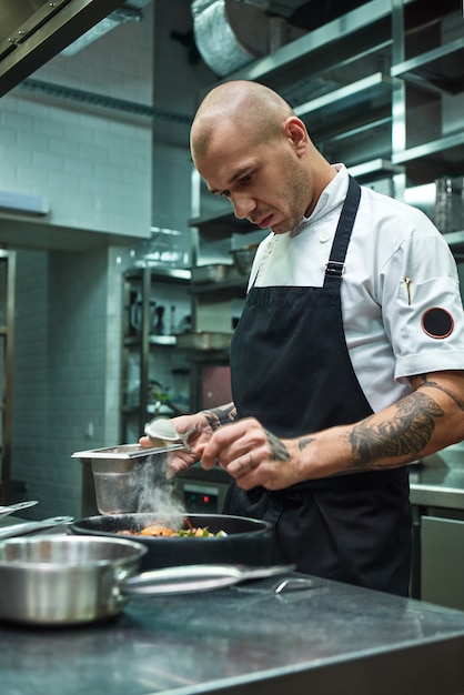 chef com várias tatuagens adicionando um tempero especial à massa fresca cozida à carbonara