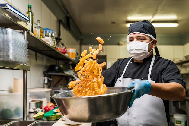 Chef condimentando papas fritas con sal en un tazón volteándolas