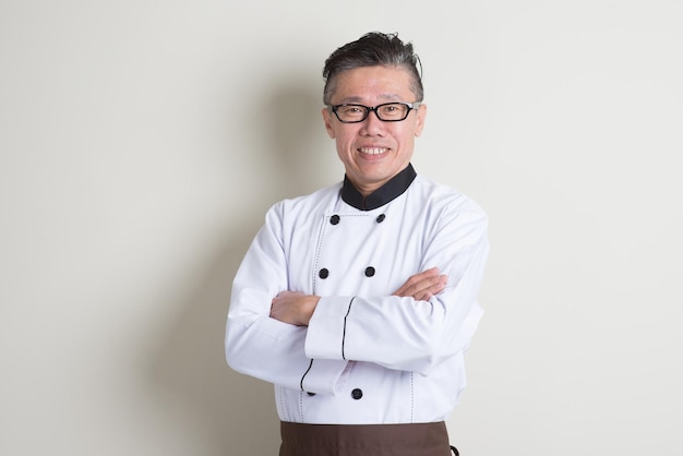 Chef confiado vestido con uniforme de pie contra la pared