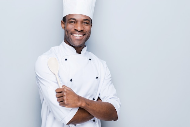 Chef confiante. Jovem chef africano alegre de uniforme branco, de braços cruzados e sorrindo