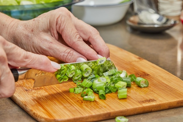 Chef corta alho-poró na tábua de madeira na cozinha