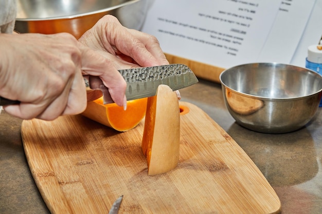 El chef corta la calabaza en forma de pera en una tabla de madera en la cocina de la casa