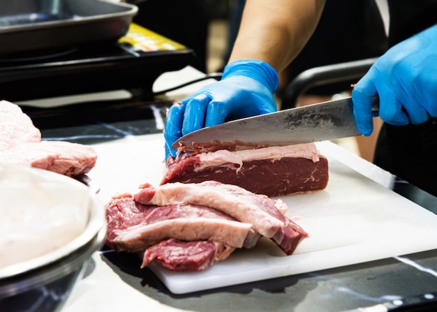 Chef corta carne cruda con un cuchillo en una tabla