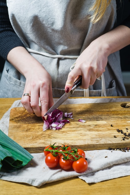 El chef corta las cebollas rojas en una tabla de cortar de madera.