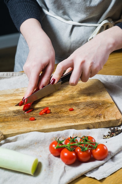 El chef corta chiles en una tabla de cortar de madera.