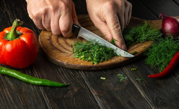 El chef corta eneldo verde fresco en una tabla de cortar con un cuchillo