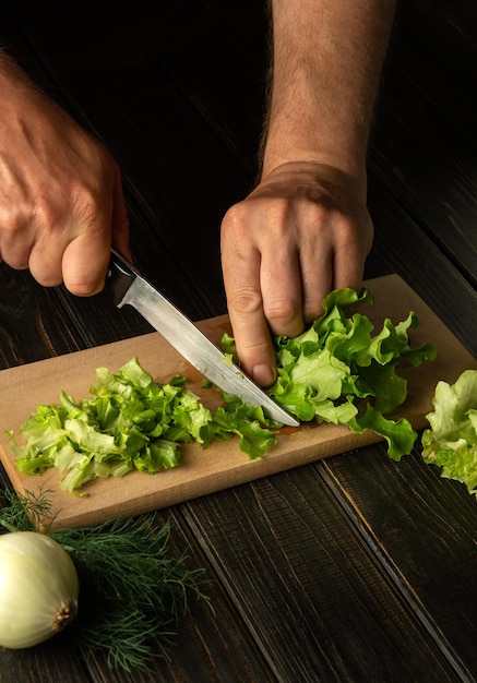 El chef corta hojas de lechuga frescas en una tabla de cortar para una ensalada de vitaminas Menú dietético para el desayuno