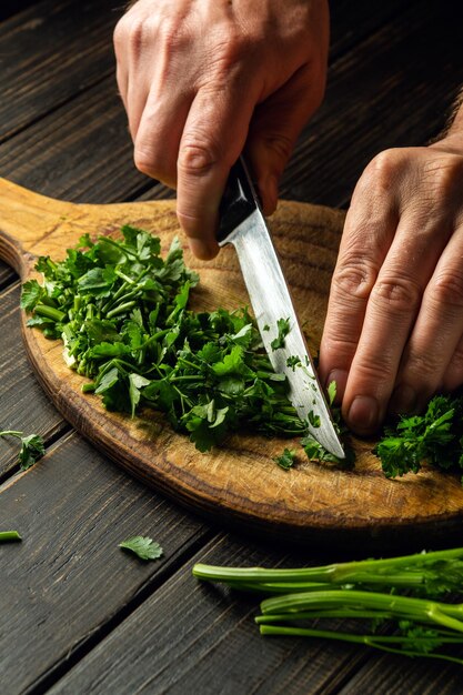 Chef corta hojas de perejil verde en una tabla de cortar con un cuchillo para preparar un plato vegetariano