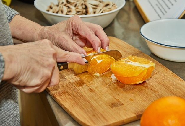 Chef corta laranjas para preparar salada com laranjas de abobrinha e cozinha gourmet francesa de salame em um fundo de madeira
