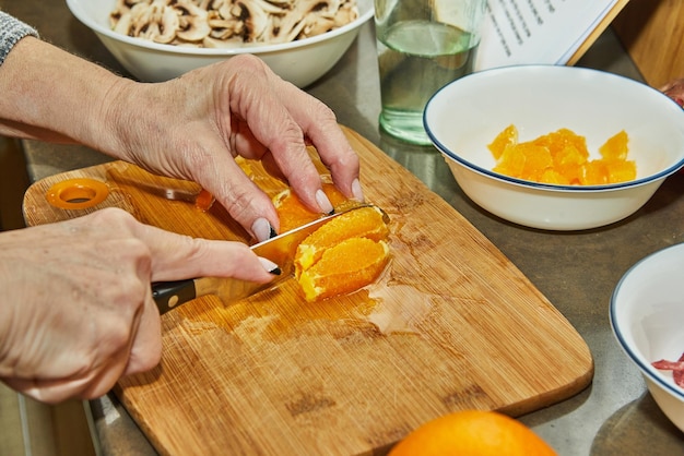 Chef corta laranjas para preparar salada com laranjas de abobrinha e cozinha gourmet francesa de salame em um fundo de madeira